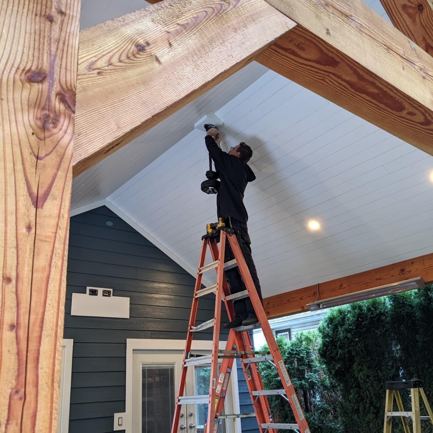 Electrician installing an outdoor ceiling fan on a covered patio
